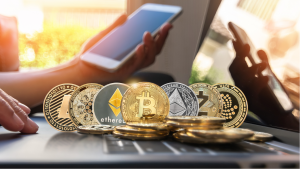 hot cryptos to buy: various cryptocurrency coins lie on a computer in front of someone holding a phone.  cryptos for huge profits.  cryptos to buy