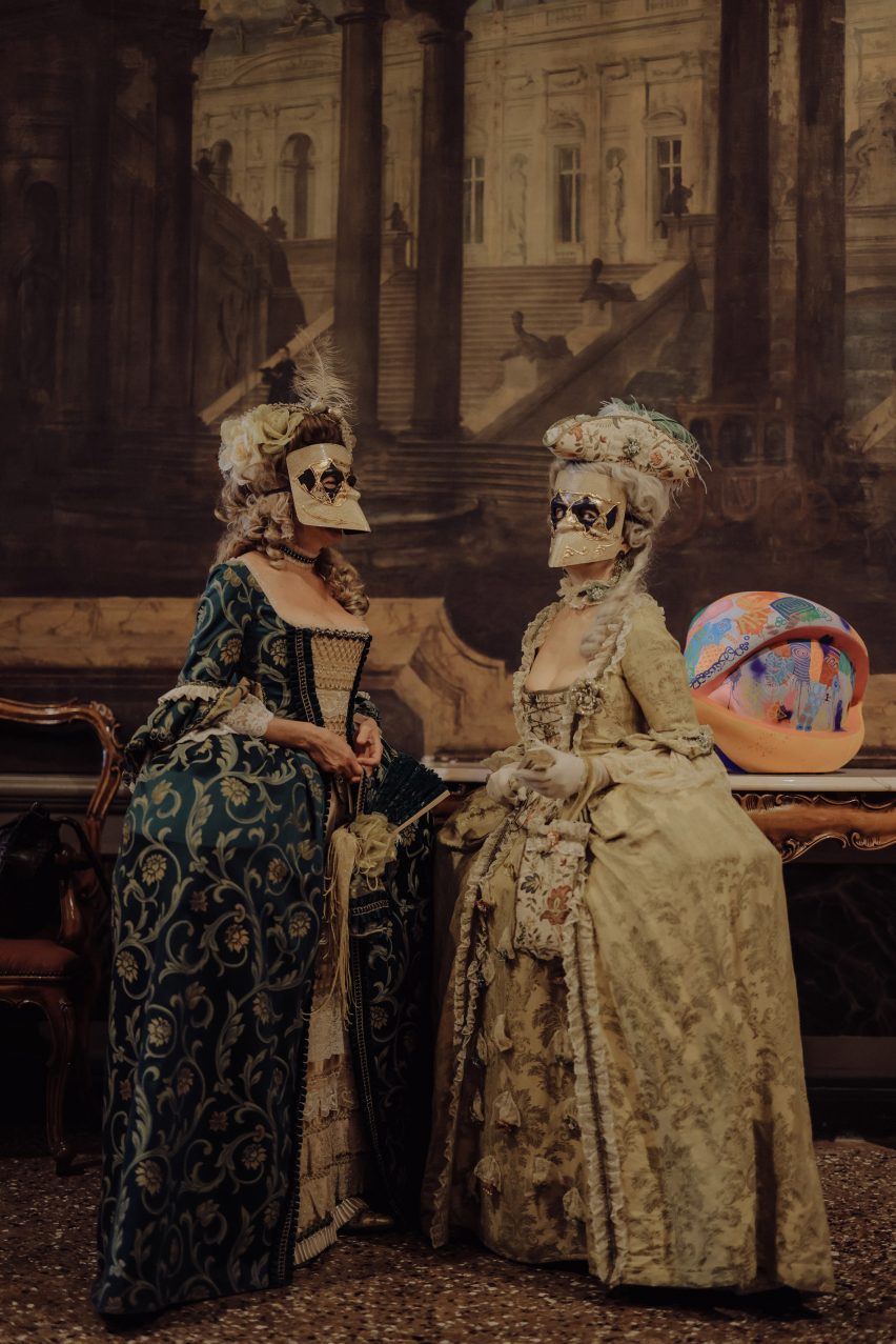 Women in traditional Venice Carnival costumes next to an eye sculpture