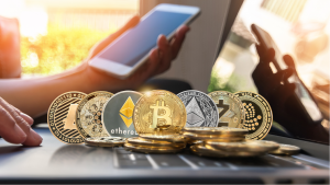 Interesting cryptocurrencies to buy: Various cryptocurrency coins are on a computer in front of someone holding a phone.  cryptocurrencies for huge profits.  cryptocurrencies to buy